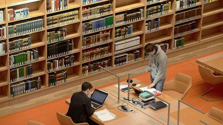 Zwei junge Männer schreiben und recherchieren in einer Bibliothek.