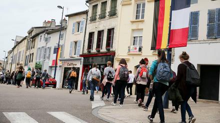 Jugendliche gehen eine Straße herunter, die mit deutschen und französischen Flaggen geschmückt ist.