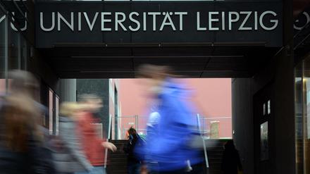 Vor dem Hauptgebäude der Universität Leipzig gehen Passanten, die nur verschwommen zu sehen sind.