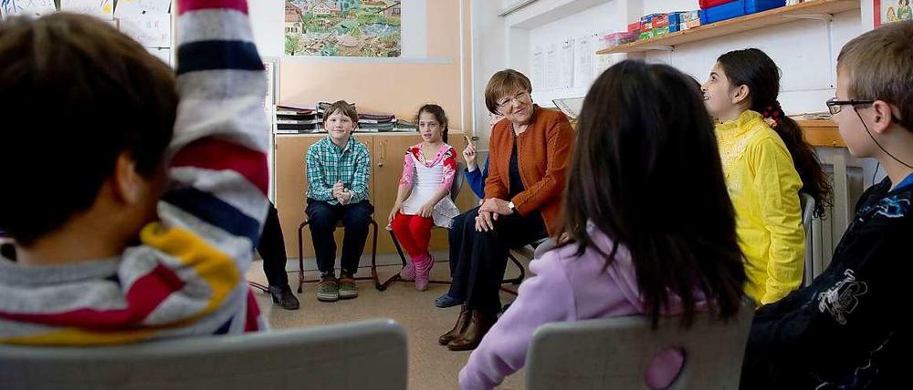 Schülerinnen und Schüler sitzen in einem Klassenraum im Kreis und sprechen mit einer älteren Frau.