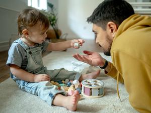 Ein Vater spielt mit seinem Sohn auf einem Teppichboden (Symbolbild)