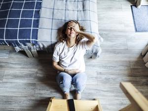 Eine junge Frau sitzt erschöpft auf dem Fußboden neben einem Bett (Symbolbild).