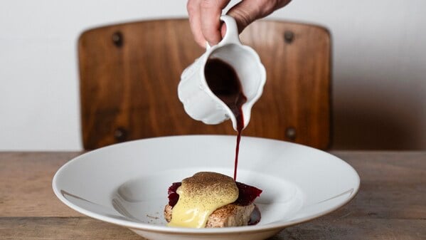 Eine Hand gieße dunkle Sauce über ein Gericht.