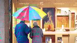 Zwei ältere Personen stehen bei Regen vor einem Schaufenster eines Schmuckgeschäfts und betrachten die ausgestellten Waren (Symbolbild).