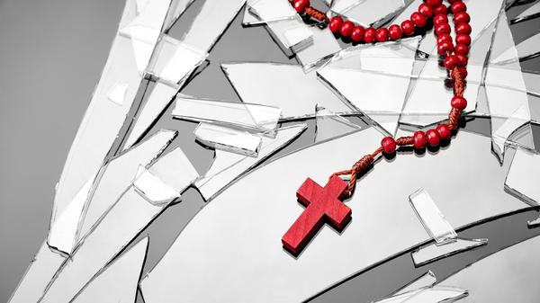 Rotes Kruzifix auf Glassplittern. Die christlichen Kirchen verlieren immer mehr Mitglieder. 