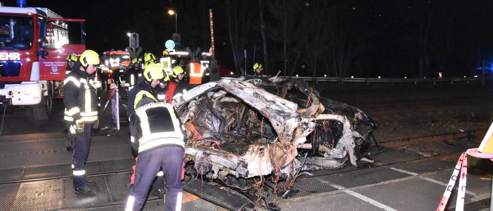 Rettungskräfte stehen am Wrack eines zerstörten Autos nach einem Unfall an einem Bahnübergang. 