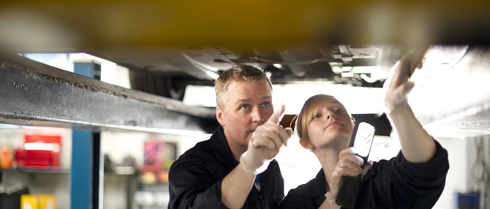 young female apprentice mechanic working under a car