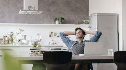 Junger Mann chillt vor Laptop in einer Küche.