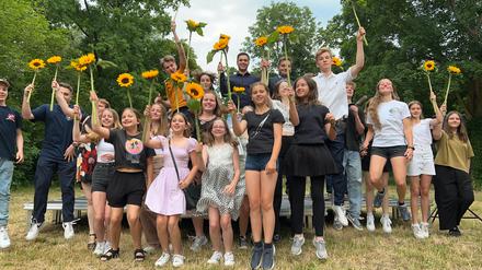 Kinder und Jugendliche, die vom Bezirksamt für ihre Engagement geehrt wurden, halten Sonnenblumen in der Hand und springen gemeinsam hoch.