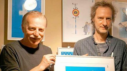 Einladung zur Karikaturenschau. Die Wettbewerbsveranstalter Valeriu Kurtu (li.) und Paul Gross mit dem Sieger-Cartoon.von Sergey Semendyaev.