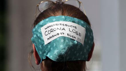 Eine Demonstrantin trägt eine Maske auf dem Hinterkopf am Rande der Demo auf dem Rosa-Luxemburg-Platz.