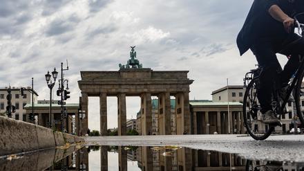 Das Brandenburger Tor spiegelt sich in einer Regenpfütze, während ein Radfahrer vorbeifährt.