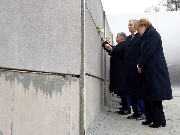 Bundeskanzlerin Merkel und der Regierende Bürgermeister Wowereit stecken an der Bernauer Straße eine Rose in einen Mauerspalt. 