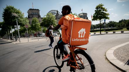 Ein Kurier des Essens Lieferdienstes Lieferando fährt mit seinem Rucksack am Sitz des Deutschen Bundestags, dem Reichstagsgebäude vorbei.