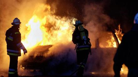 Feuerwehrmänner löschen ein brennendes Auto - Symbolbild.