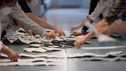 Hände von Wahlhelfern und Wahlhelferinnen auf einem Tisch beim Zählen von Stimmzetteln in einem Wahllokal.