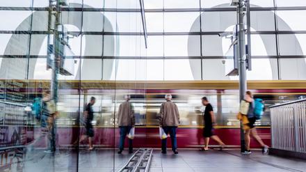 Eine S-Bahn fährt am Berliner Bahnhof Ostkreuz ein und spiegelt sich in einer Glasscheibe.