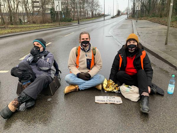 Drei Aktivisten am Mittwochnachmittag an der Auffahrt zur A103 in Steglitz - rechts Lea Bonasera, die Hand auf den Asphalt geklebt.