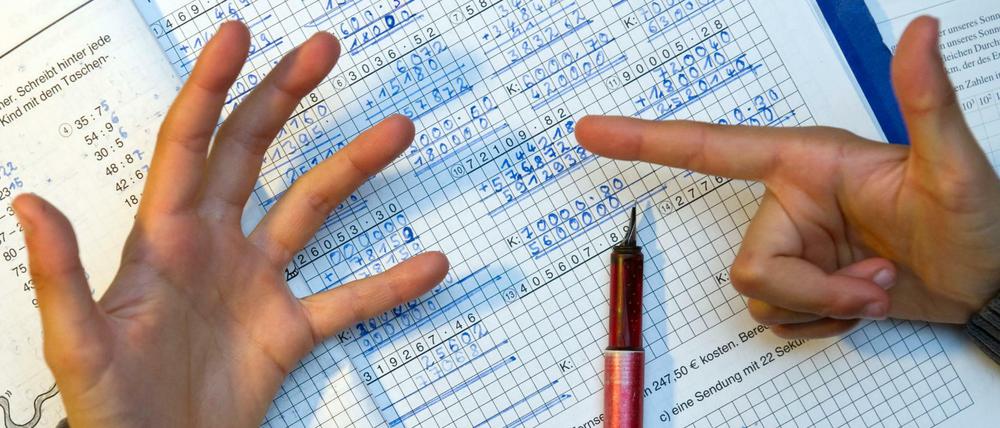 Ein Junge nimmt bei den Hausaufgaben im Fach Mathematik seine Finger zur Hilfe um besser zählen zu können.