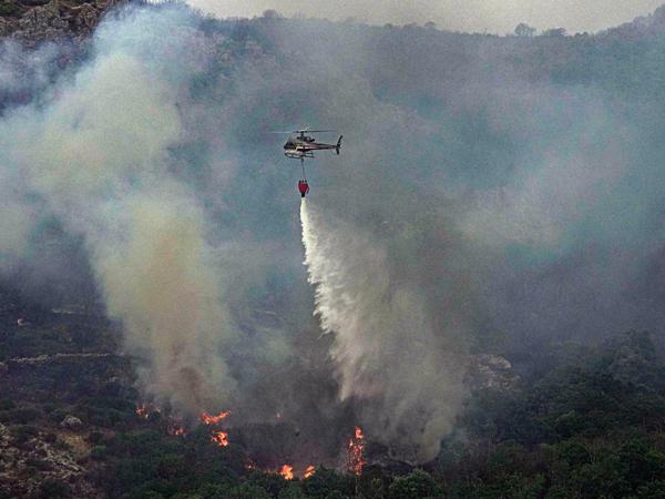 Ein Hubschrauber wirft über einem Waldgebiet in Cugliari Wasser ab, um Flammen zu löschen.