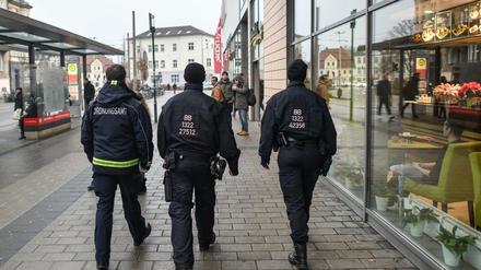 Ein Mitarbeiter des Ordnungsamtes und zwei Beamte der Bereitschaftspolizei gehen auf Streife vor dem Einkaufszentrum in Cottbus (Brandenburg).