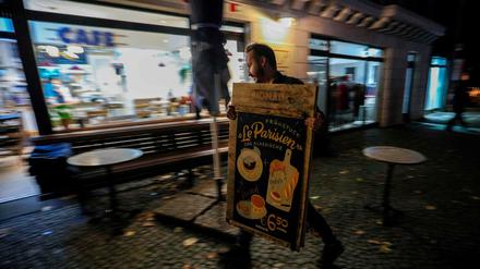 Der Berliner Café-Betreiber John Bleys räumt am Sonntagabend einen Aufsteller ab, um seinen Laden für einen Monat zu schließen. Das sehen die jüngsten Auflagen zur Bekämpfung der Pandemie vor, die das Abgeordnetenhaus am Sonntag in einer Sondersitzung verabschiedet hat.