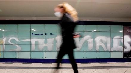 Eine Frau mit Mund-Nasen-Schutz geht am U-Bahnhof Amrumer Straße in Berlin an einem Graffiti vorbei.