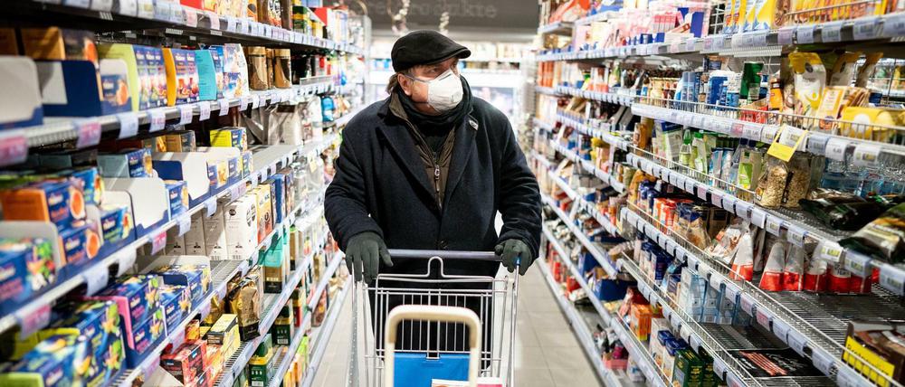 Ein Kunde kauft mit Mundschutz und Handschuhen am frühen Morgen in einem Supermarkt im Berliner Stadtteil Friedenau ein.