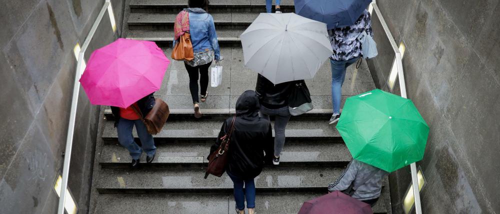 Menschen mit bunten Regenschirmen, die eine Treppe in Berlin hinaufgehen, von oben fotografiert.
