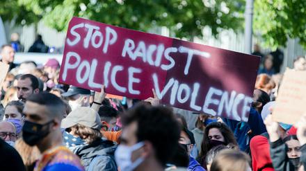 Teilnehmende einer Kundgebung in Berlin halten ein Plakat mit der Aufschrift: "Rassistische Polizeigewalt stoppen".