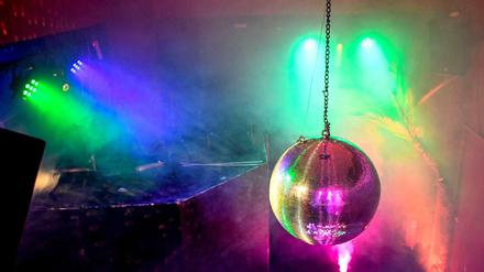 Eine Diskokugel dreht sich in einem Club und reflektiert das einfallende Licht der Scheinwerfer und Lampen. 