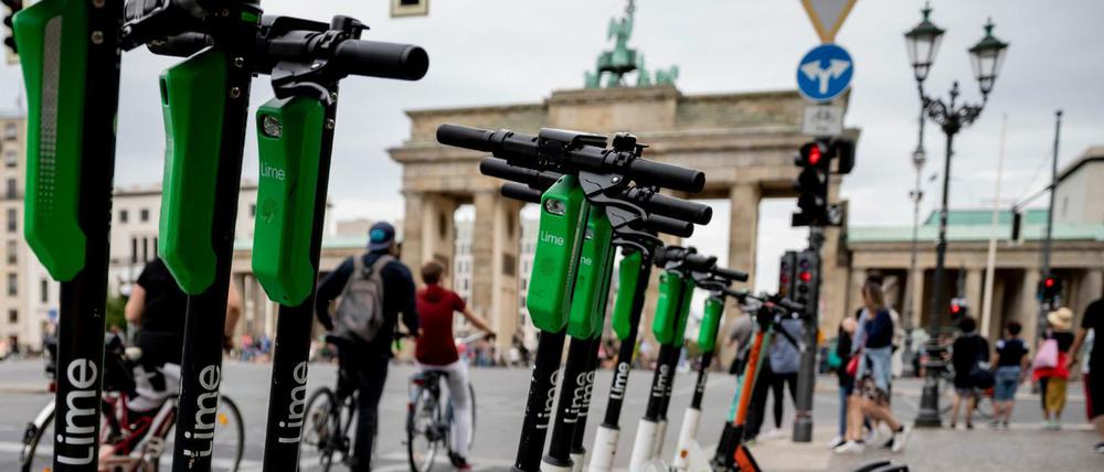 E-Tretroller stehen vor dem Brandenburger Tor am Rand der Straße des 17. Juni geparkt, während Fahrradfahrer an der Ampel warten.