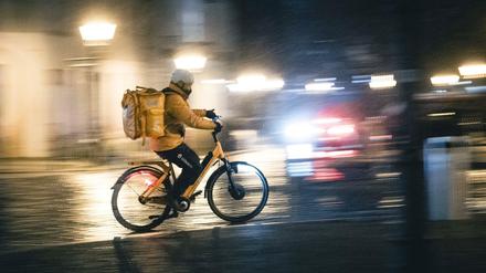 Ein Lieferbote auf einem Fahrrad fährt bei Regen durch Berlin. 