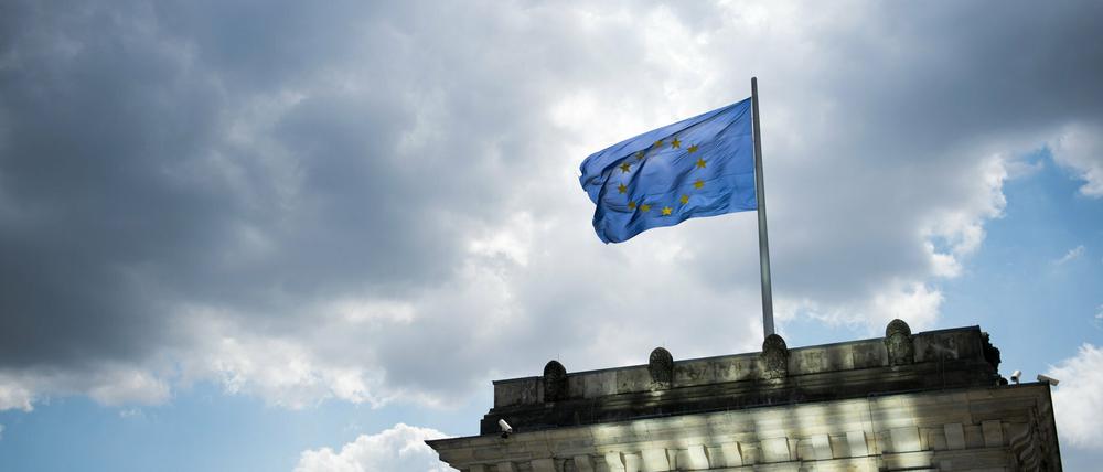 Eine Europaflagge weht am auf dem Dach des Reichtagsgebäudes in Berlin. Es bleibt bewölkt.