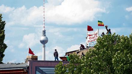 Seit dem Sommer 2014 ist die Gerhart-Hauptmann-Schule in Kreuzberg von Flüchtlingen besetzt. Hier sieht man einige bei Protesten auf dem Dach im Juni desselben Jahres.