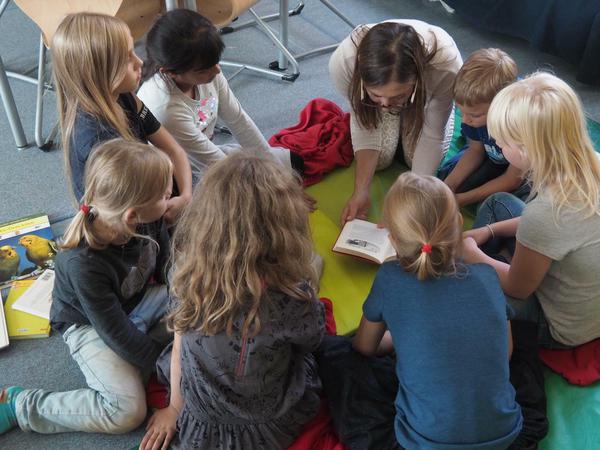 Kinder sitzen um Bianca Böttcher herum und lauschen beim Vorlesen.