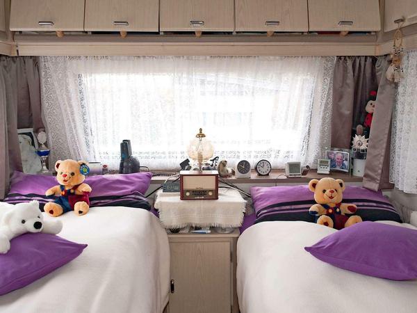 Ein Blick in den Wohnwagen: Zwei Betten mit lila Kopfkissen, auf beiden Betten sitzen Stoffteddybären.