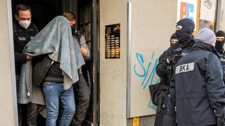 Ein Mann wird bei einer Razzia in Berlin, mit einer Decke über dem Kopf, von der Polizei abgeführt. 