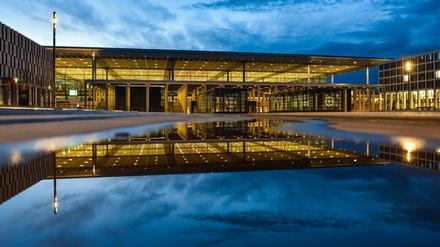 Das Terminalgebäude des beleuchteten Hauptstadtflughafens Berlin Brandenburg (BER) spiegelt sich in einer Pfütze. 