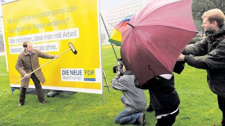 Nass gemacht. FDP-Chef Christoph Meyer klebt – im  Regen stehend und umtost von Autokarawanen am Ernst-Reuter-Platz – die ersten Plakate. Foto: dpa/Gambarini