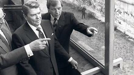 Noch 881 Tage. So lange dauerte es nach Reagans Besuch, bis die Mauer fiel. Hier wirft er vom Reichstag aus einen Blick darauf, flankiert von Kohl (li.) und Diepgen.