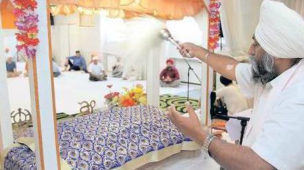 Gut gefächelt. Das heilige Buch der Sikh liegt während des Gottesdienstes im Reinickendorfer Tempel auf einem Bett. Ein Gemeindemitglied fächelt ihm Luft zu. Foto: Davids/Darmer
