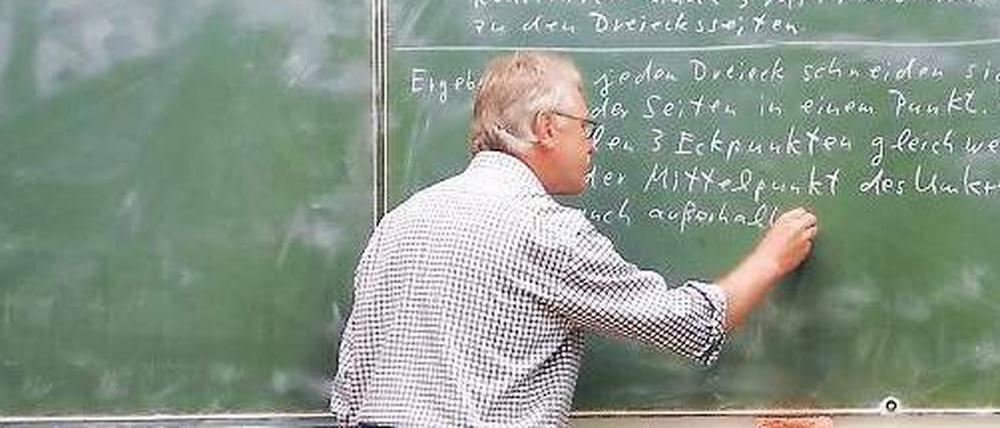 Ein Lehrer schreibt eine mathematische Formel an die Tafel.