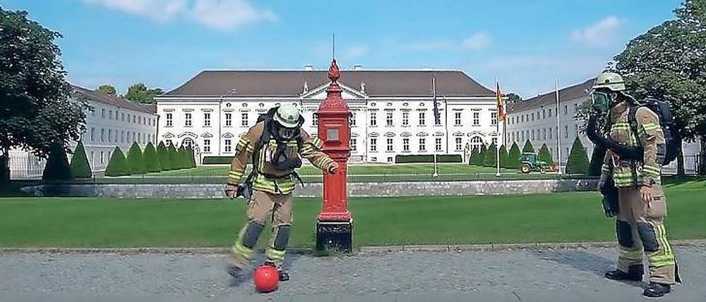 Berliner Feuerwehrleute kicken einen roten Ball vor dem Schloss Bellevue.