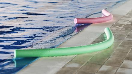 Green and pink foam aqua noodles placed near swimming pool for water aerobics training
