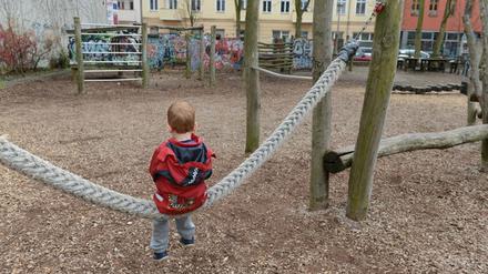 Ein fünfjähriger Junge sitzt allein auf einer Schaukel auf einem Abenteuerspielplatz in Berlin.