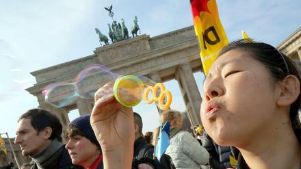 Menschen bei der Demonstration "Vergesst Fukushima nicht!" vor dem Brandenburger Tor. Eine Teilnehmerin bläst Seifenblasen.