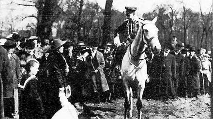 Kronprinz Wilhelm auf einem Pferd im Gespräch mit einem Kindermädchen, umgeben von einer Menschenmenge.