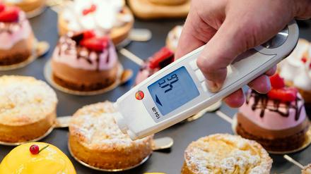 Ein Lebensmittelkontrolleur hält in einer Patisserie ein Thermometer an eine kleine Torte.