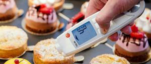 Ein Lebensmittelkontrolleur hält in einer Patisserie ein Thermometer an eine kleine Torte.